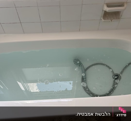אמבטיה מלאה במים עם ראש מקלחת וכיסוי קרמיקה